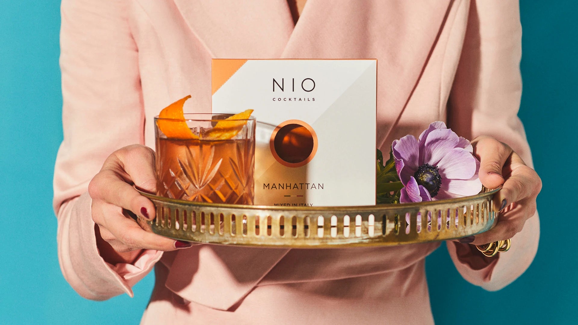 lady in pink elegant dress serving tray with manhattan nio cocktail pack and glass
